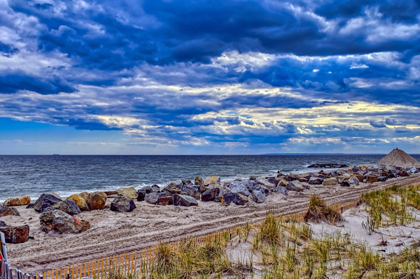 Dune, beach grass, and jetty on the Lewes shoreline under a dramatic sky